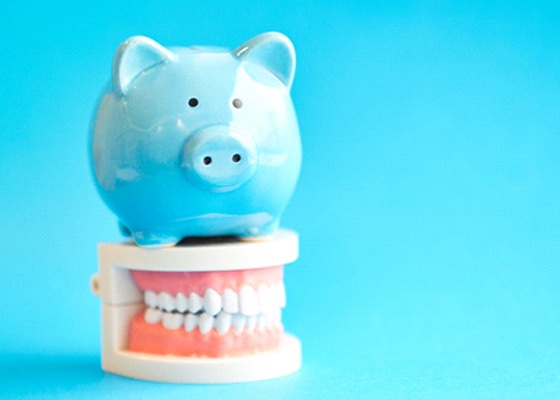 Piggy bank atop model teeth representing the cost of smile makeovers in Annapolis