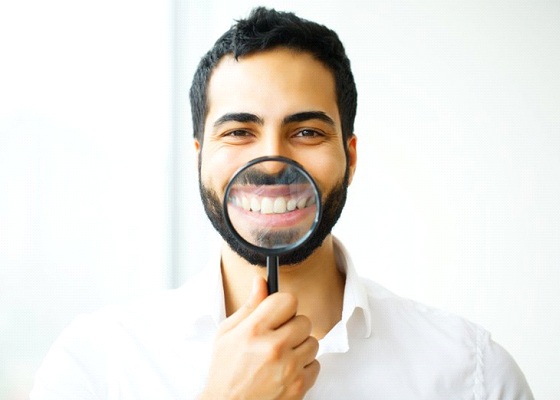 man holding magnifying glass to his smile after teeth whitening in Annapolis